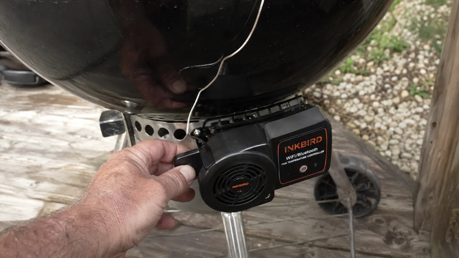 Close-up of the Inkbird fan controller unit clipped onto the bottom vent of a charcoal kettle grill