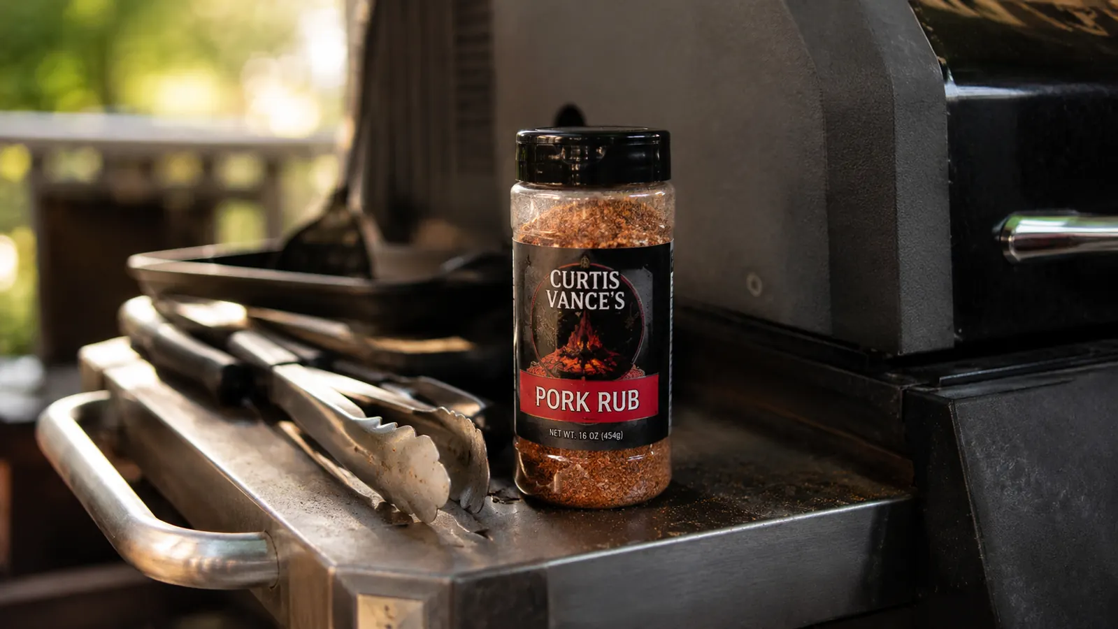 A single large bottle of barbecue rub standing on a metal grill cart shelf, clearly well used