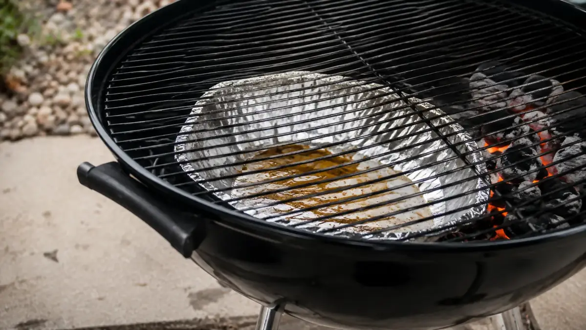 Homemade foil catch pan molded by hand and set under a charcoal kettle grill